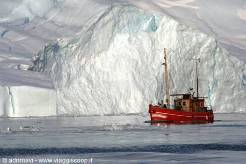 Small red wooden boat moored in front of a huge glowing iceberg in Antarctica