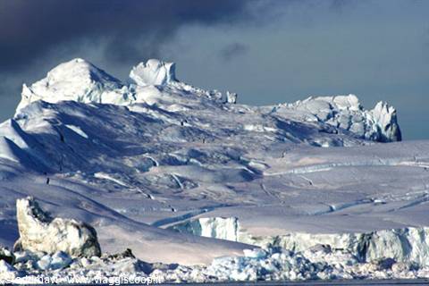 Massive icebergs of blue ice under cloudy sky, cold light on water