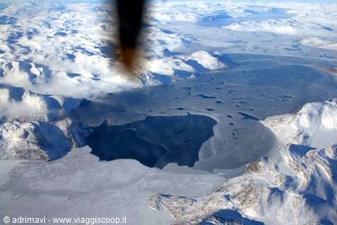 Frozen sea amid snowy mountains, photographed from aircraft, cold light