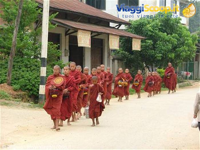 Line of Buddhist monks in red robes with alms bowls walking on dirt road