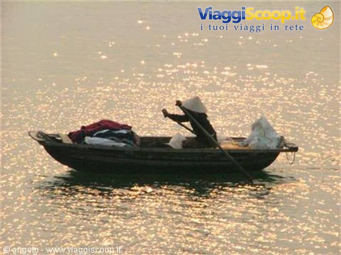 Wooden boat with conical-hat fisherman rowing on shimmering golden water