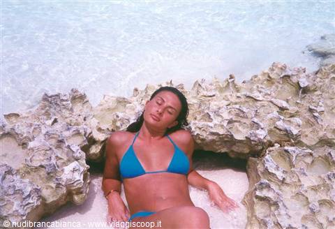 Woman in blue bikini lying on limestone rocks in turquoise water