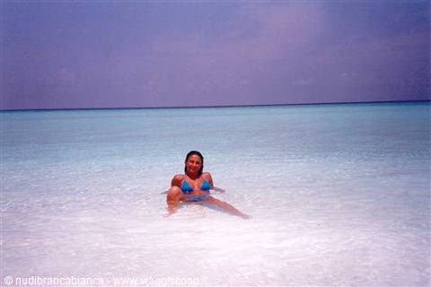 Woman in blue bikini sitting in shallow turquoise water on white sand