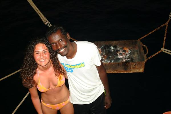 Smiling tourist and man beside charcoal grill suspended on a boat