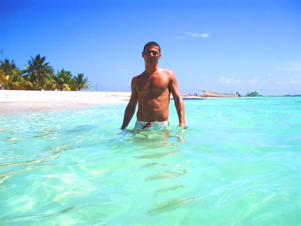 Man in turquoise sea with boats and palm trees on sunny beach