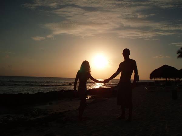 Couple silhouetted hand in hand on the beach, low sun over the sea