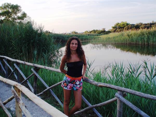 Girl leaning on a wooden fence by a pond with reeds