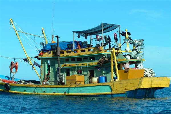 Green and yellow wooden fishing boat loaded with nets and gear at sea
