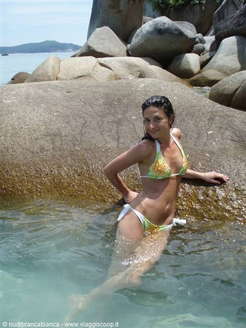 Woman in bikini posing in turquoise water among large granite boulders