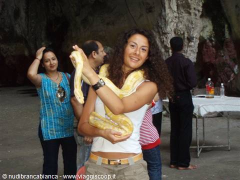 Smiling girl holding a large yellow python around her neck inside a cave