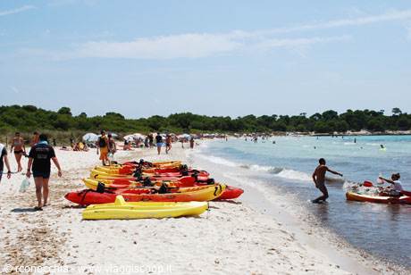 Colorful kayaks on white sand, bathers and a boy playing with a ball