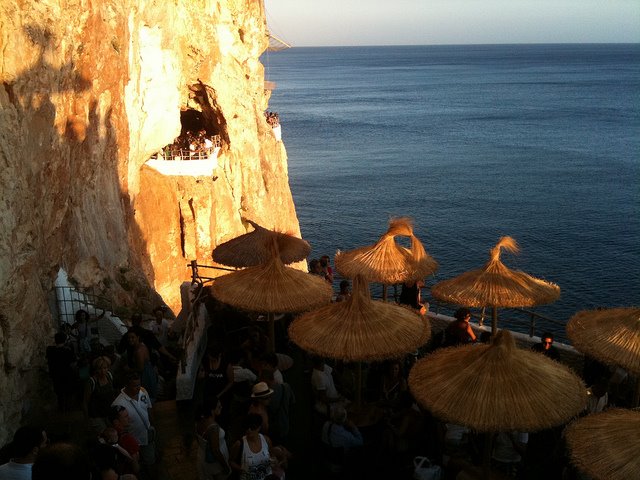 Straw umbrellas on a cliffside terrace carved in rock, Cova d'en Xoroi