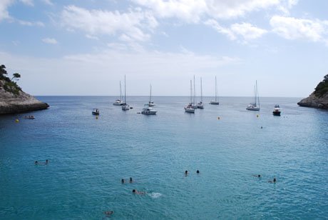 Swimmers and anchored sailboats in a turquoise cove between white cliffs