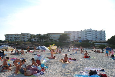 Beachgoers on white sand with umbrellas, hotels and pines behind