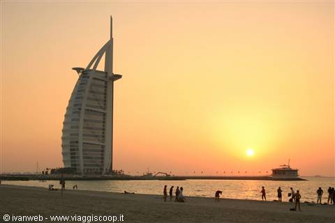 Tourists on the beach at sunset in front of Dubai's Burj Al Arab