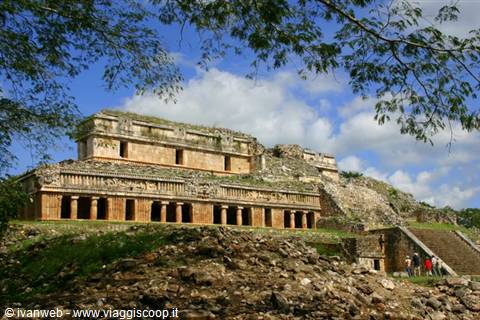 Stone Maya temple at Sayil, carved columns on green hill under white clouds