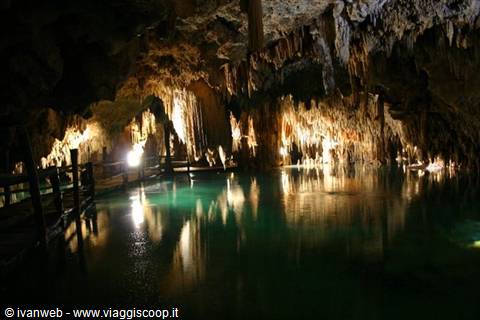 Illuminated stalactite cave over underground turquoise water, wooden walkway