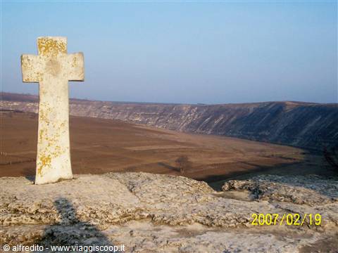 White stone cross on rock above plowed fields and limestone cliffs, Orheiul Vechi
