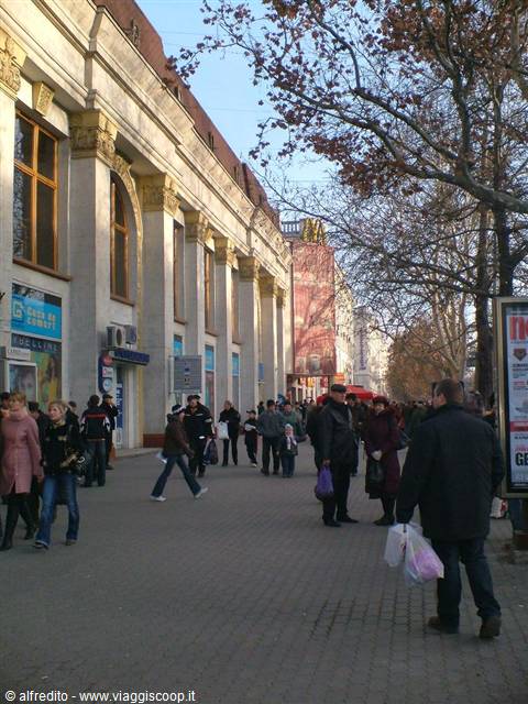 People walk along cobbled avenue beside building with columns