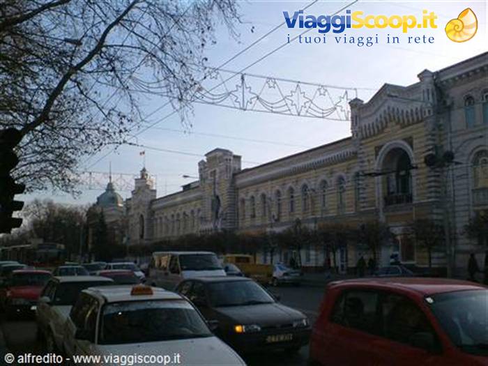 Traffic in front of a yellow historic building with Christmas decorations overhead