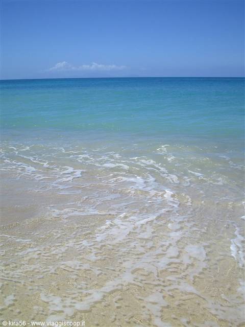 Turquoise water and foam on pale sand, blue sky with distant clouds