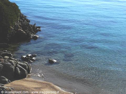 Granite rocks and sand meet clear turquoise water,green vegetation on the left