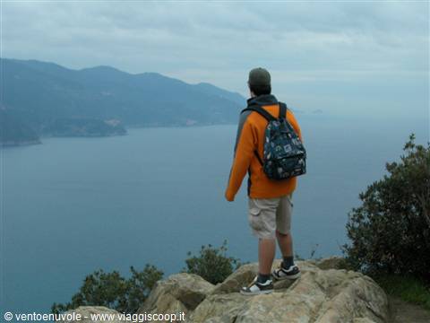 Boy with orange backpack standing on rocks overlooking the Ligurian sea