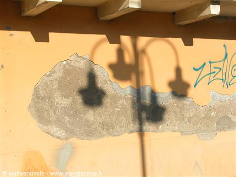 Street lamp shadow on ochre wall with peeling plaster and blue graffiti