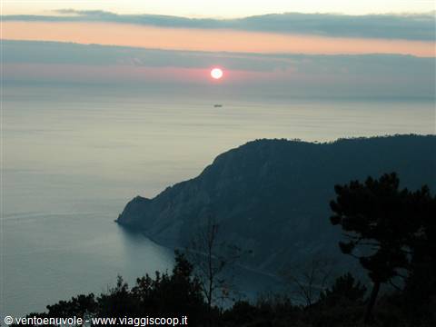 Sun rising over the sea behind the dark cliff of Monte Rosso, Cinque Terre