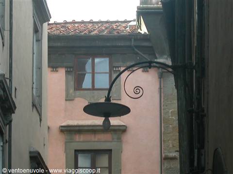 Wrought iron street lamp before a pink building among narrow alleys