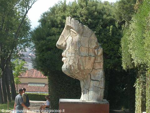 Cracked stone giant head in Boboli Gardens, surrounded by trees and visitors