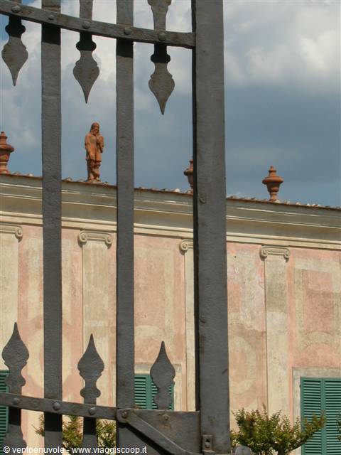 Wrought iron gate in front of pink facade with terracotta statues on the roof
