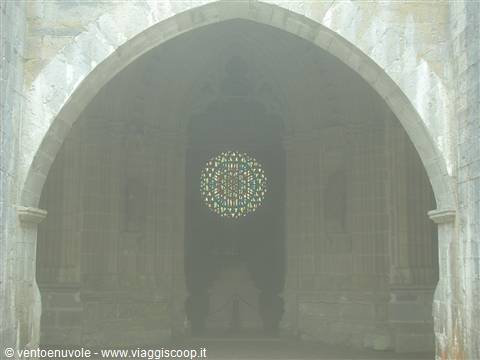 Large stone arch in the fog with a glowing rose window behind