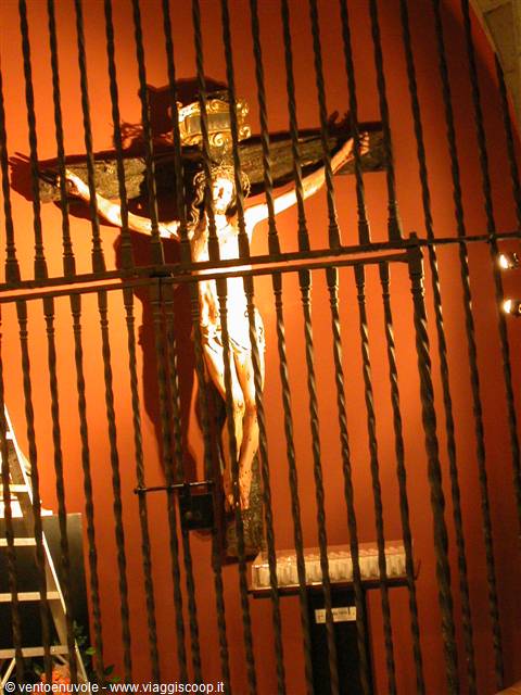 Wooden crucifix behind a wrought iron gate, lit against a red wall