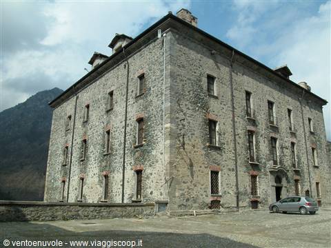 Old grey stone building under cloudy mountains, a car parked beside it