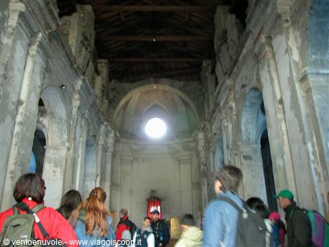 Visitors with backpacks inside a ruined church nave, light through the oculus