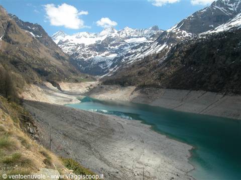 Nearly empty alpine reservoir with turquoise water among snowy mountains