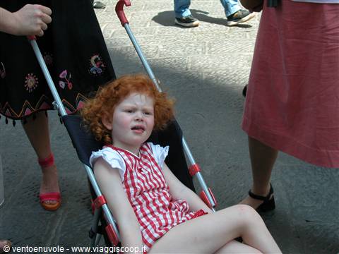 Curly red-haired girl in red checkered dress lying in a stroller