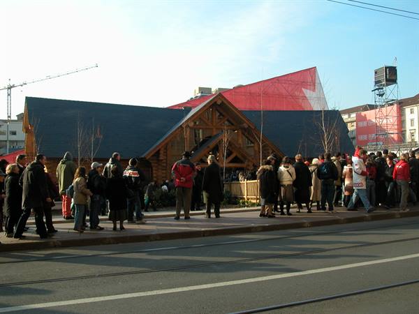 Crowd outside a wooden chalet with a large Swiss flag, winter light