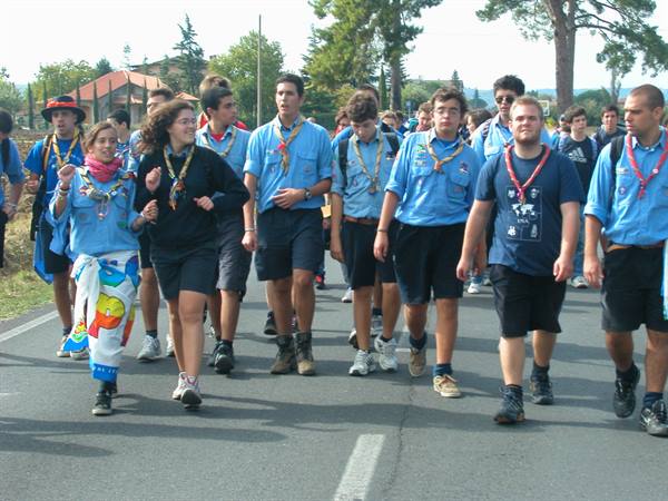 Group of scouts with neckerchiefs marching along a paved road among trees