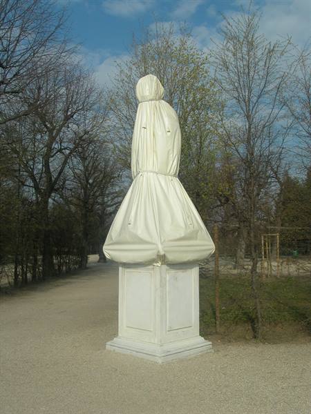 Statue wrapped in white cloth on stone pedestal, tree-lined park