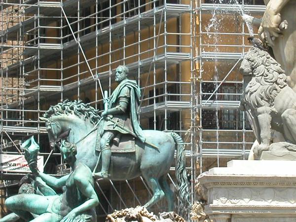 Bronze equestrian statue before scaffolding, beside marble lion and triton