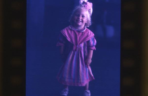 Smiling little girl in pink dress with hair bow, soft light