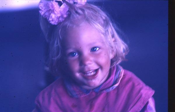 Smiling blonde child with pink bow in her hair, bright light on face