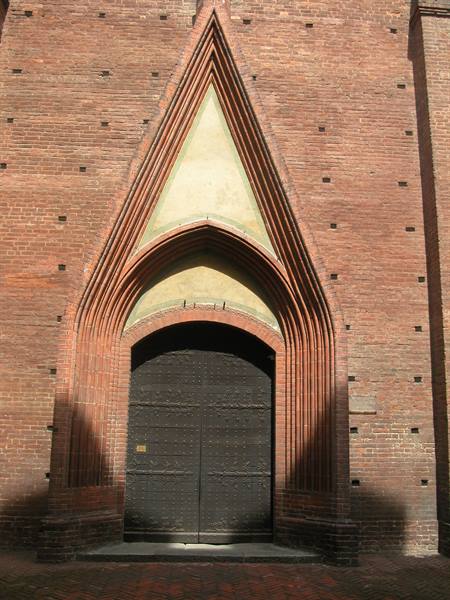 Dark wooden door beneath red brick Gothic arches in sunlight