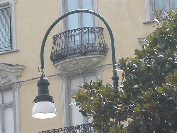 Curved green streetlamp in front of yellow building with wrought-iron balcony