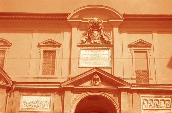 Brick façade with papal coat of arms, inscription plaque and archway, orange tone