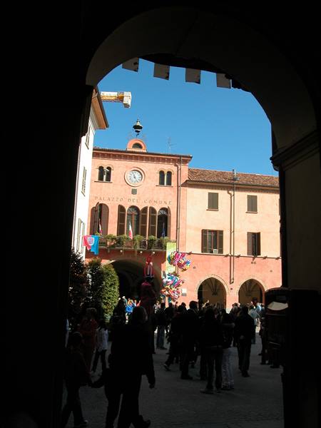 People walking beneath an arch in front of the Palazzo del Comune