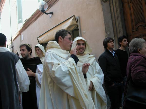 Men in white hooded robes parade along a street among onlookers