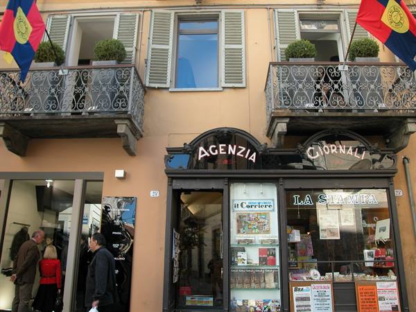 Newsstand with Agenzia and Giornali signs under wrought-iron balconies with flags